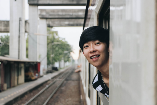 Kid smiling out a train window and wearing braces on his teeth.