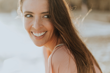 A woman at the beach smiling towards the camera wearing Invisalign clear aligners